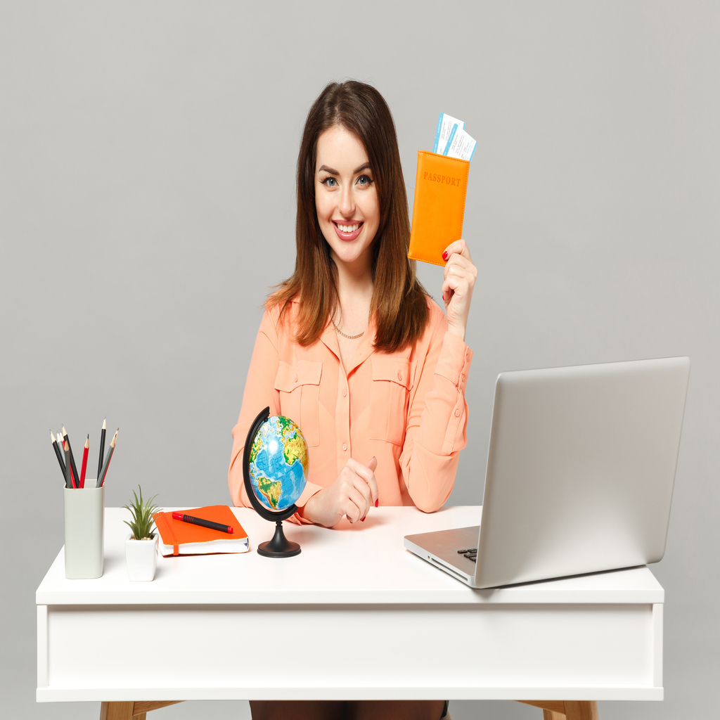 Young smiling woman holding Earth world globe, passport boarding pass ticket work at desk with pc laptop isolated on gray background. Achievement business career lifestyle concept. Mock up copy space